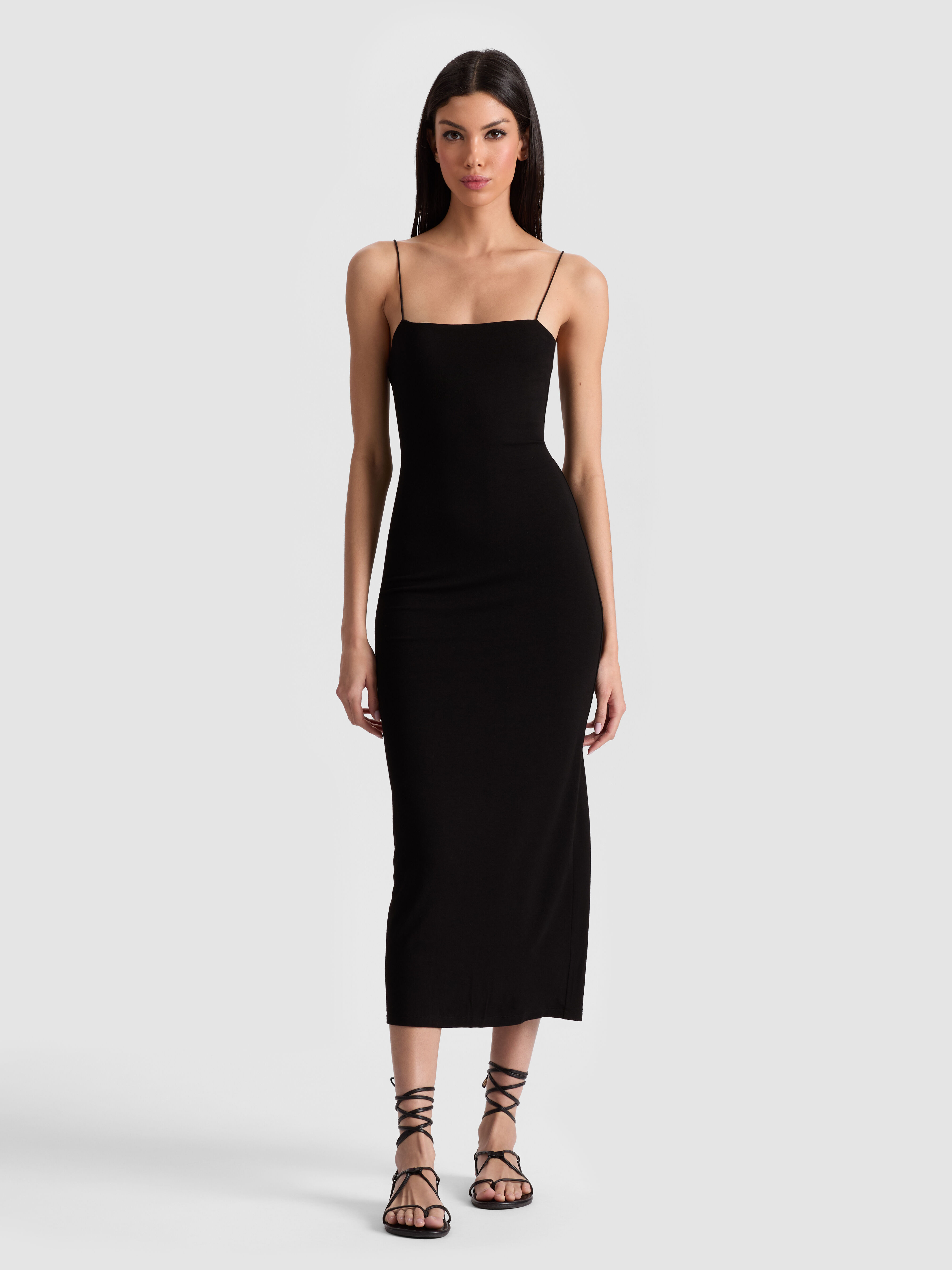 A woman wearing the FIFI MIDI DRESS — a sleek black bodycon midi with spaghetti straps and a back slit — styled with pointed-toe pumps for a sophisticated evening occasion.