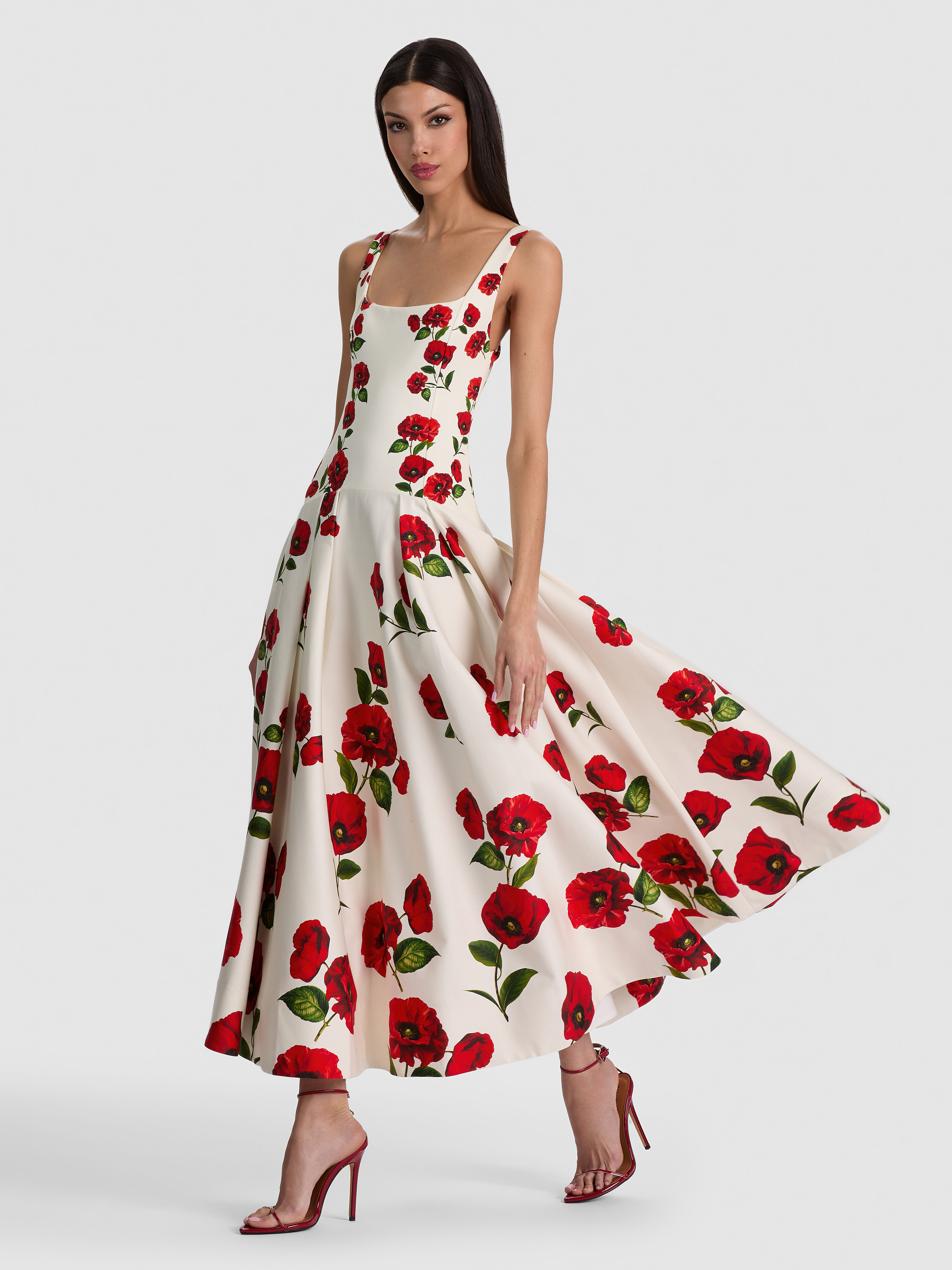 A lifestyle image of a woman wearing the ADLEY DROP WAIST DRESS with a softly pleated skirt in printed cotton sateen, styled with heels and understated accessories for an elevated daytime event.