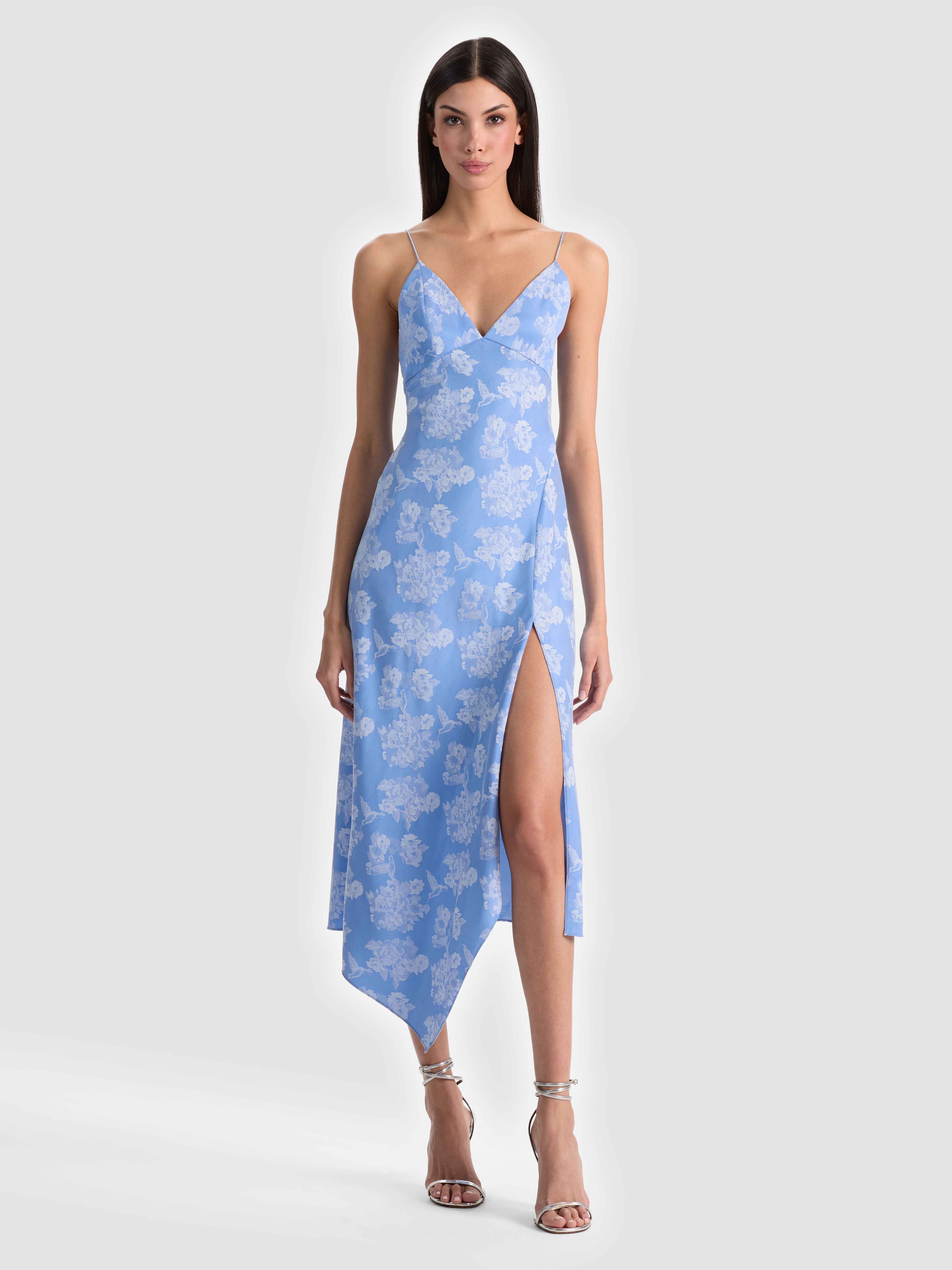A model wearing the ALICE + OLIVIA Julietta Midi Slip Dress in bold floral printed jacquard with a V-neckline, styled with gold hoops and heels for a statement look.