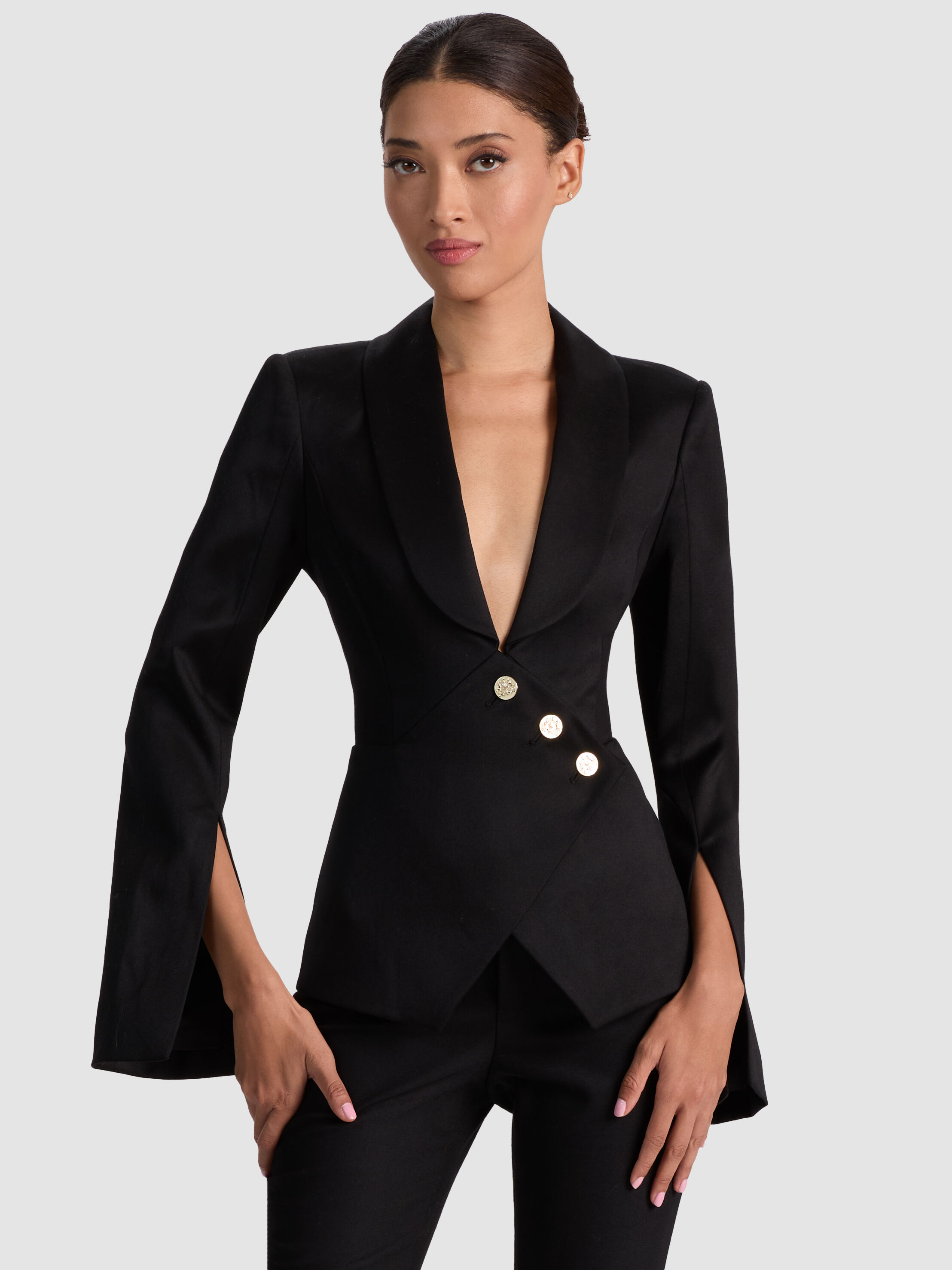 A woman wearing the ALICE + OLIVIA Sculpt Blazer styled with wide-leg pants and statement accessories — showcasing the blazer's sharp shoulder structure and asymmetric wrap front.